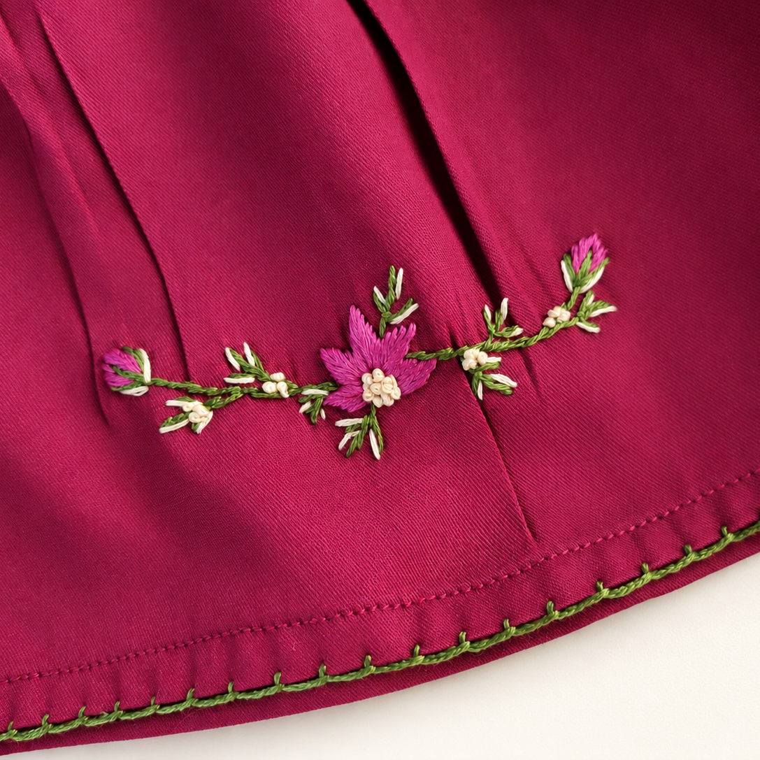 Floral hand embroidery and green edging on the deep red dress hem