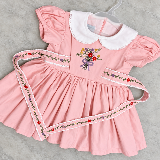 Flat lay of blush pink cotton linen hand embroidered dress with lace collar and floral embroidered sash