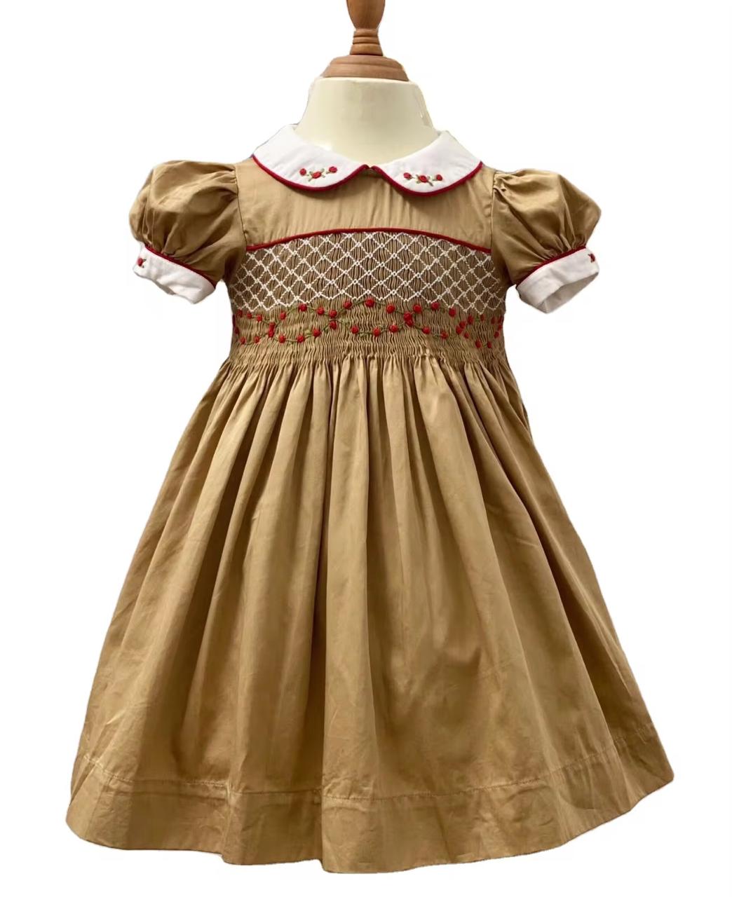 Full front view of golden caramel hand smocked dress with red piping and white Peter Pan collar on mannequin