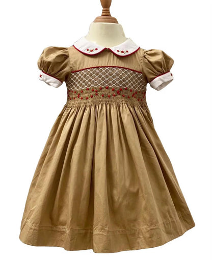 Full front view of golden caramel hand smocked dress with red piping and white Peter Pan collar on mannequin