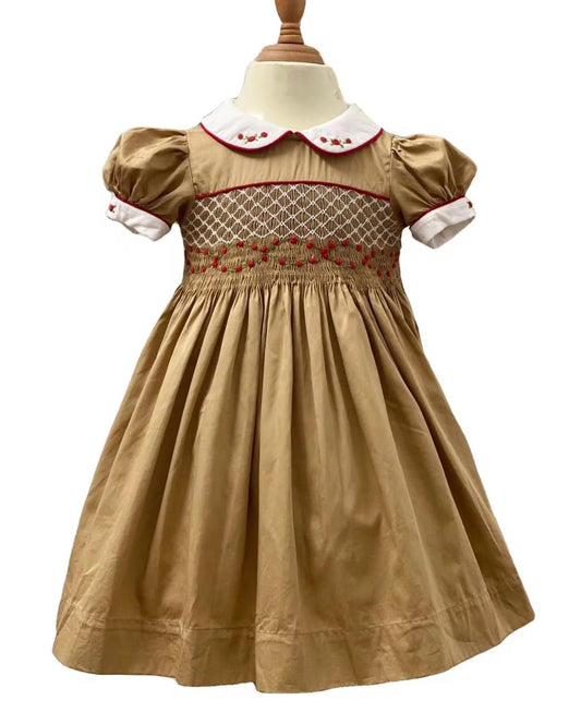 Full front view of golden caramel hand smocked dress with red piping and white Peter Pan collar on mannequin