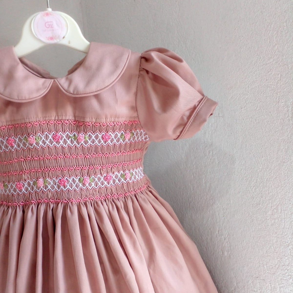 Close-up of hand smocked bodice panel with hand embroidered pink roses and diamond lattice