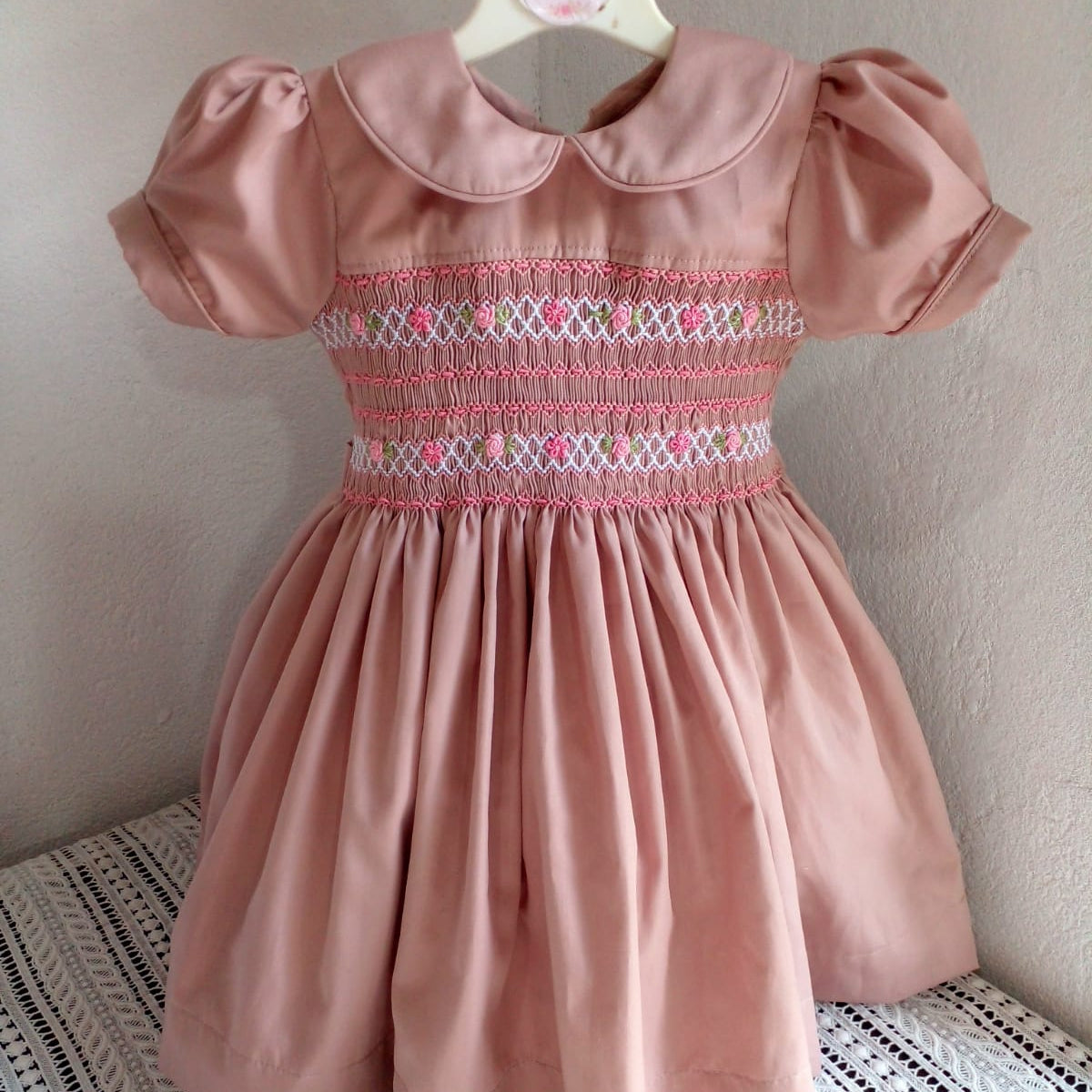 Full front view of dusty rose hand smocked and embroidered cotton girls dress on hanger