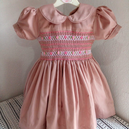 Full front view of dusty rose hand smocked and embroidered cotton girls dress on hanger